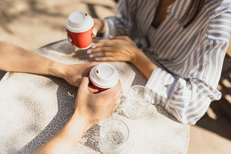 Cropped portrait of young beautiful couple sitting at cafe and enjoying coffee together outside on bright summer dayの写真素材