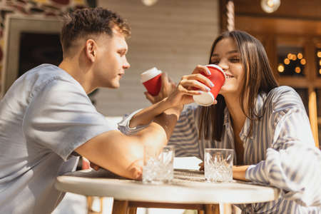 Cropped portrait of young beautiful couple sitting at cafe and enjoying coffee together outside on bright summer dayの写真素材
