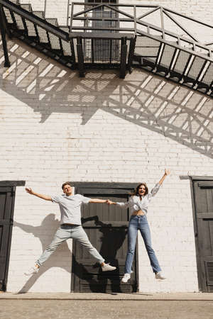 In jump. Full-length portrait of young beautiful couple spending time together outside on bright summer dayの写真素材