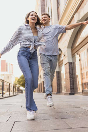 Full-length portrait of young laughing couple in motion. Walking around city on warm sunny dayの写真素材