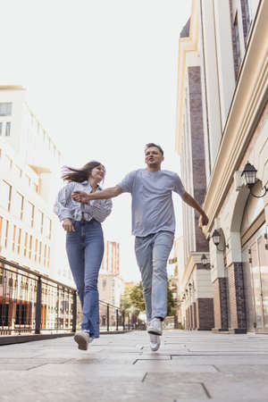 Full-length portrait of young happy couple in motion. Walking around city on warm sunny dayの写真素材