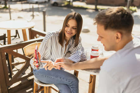 Beautiful young smiling woman showing pictute to her boyfriend on phoneの写真素材