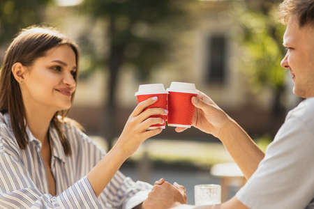 Cropped portrait of young beautiful couple sitting at cafe and enjoying coffee together outside on bright summer dayの写真素材