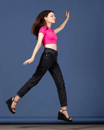 Full-length portrait of young attractive caucasian girl in motion isolated on dark blue background