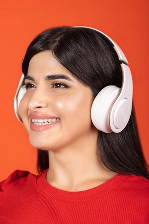 Close-up cropped portrait of of young beautiful girl in headphones isolated over orange background.