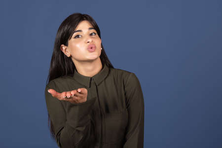 Air kiss. Cropped portrait of young beautiful expressive girl isolated on blue studio background