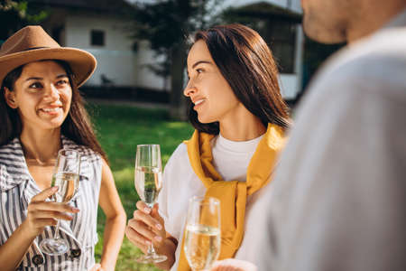 Cropped portrait of two young woman holding glass of champaing and resting with friends in...