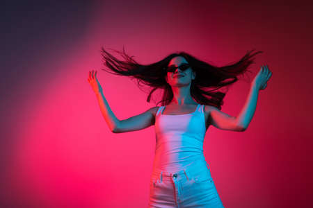 Motion shot. Cropped studio portrait of young beautiful caucasian girl on gradient pink red backgroundの写真素材