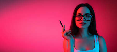 Cropped portrait of young beautiful girl in glasses on gradient pink red background