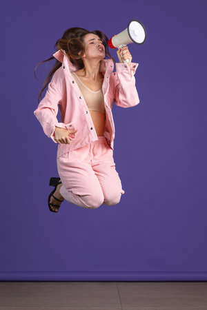 Full-length portrait of young emotional girl jumping over purple studio backgroundの写真素材