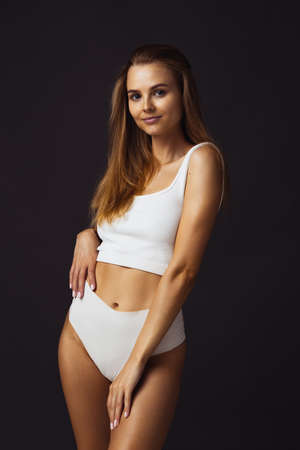 One young beautiful caucasian woman in white underwear on dark studio backgroundの写真素材