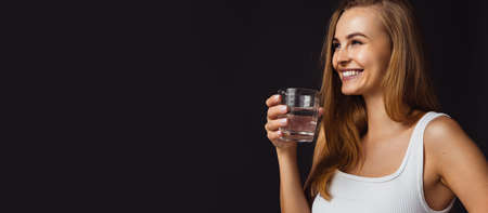 Cropped horizontal image of young beautiful smiling caucasian girl on dark studio background