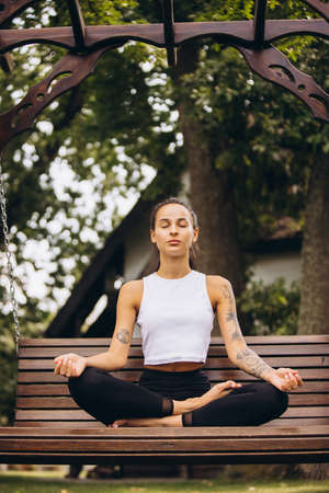 Full-length vertical portrait of young beautiful slim caucasian girl doing meditation on bench outdoorsの写真素材