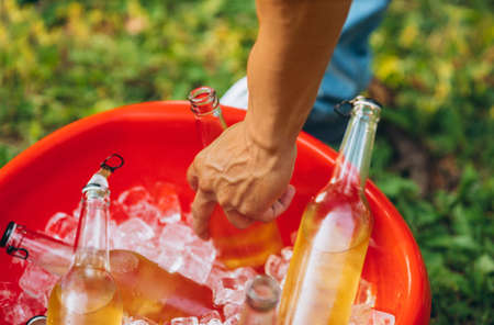 Cropped image of male hand taking bottles of beer in ice cub. Picnic gathering in countryside. Summer day offの写真素材