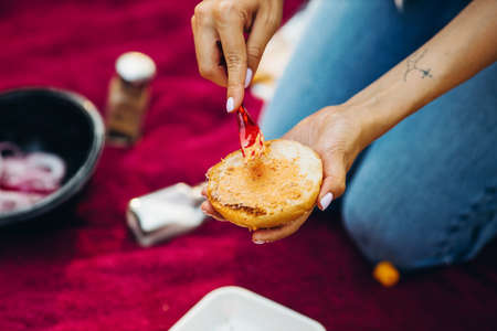 Close-up image of girl hand putting sauce on burger bun. Barbecue party outdoorsの写真素材