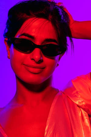 Close-up cropped image of young beautiful girl in trendy black sunglasses isolated over neon purple backgroudの写真素材