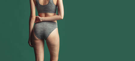 Cropped female body in gray cotton underwear over green background. Back view bodyの写真素材
