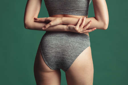 Close-up cropped image of fit female body in gray cotton underwear over green background. Back view bodyの写真素材