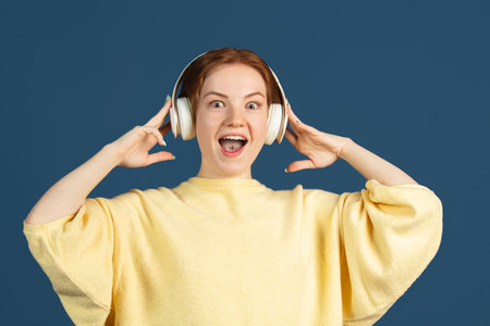 Cropped portrait of young female model with headphones isolated over dark studio backgroundの写真素材