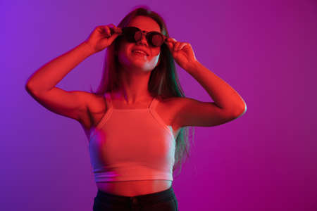 Portrait of young beautiful girl posing isolated over gradient background in neon lightsの写真素材