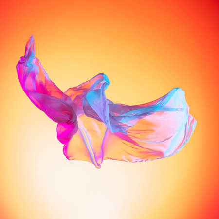 Elegant transparent multicolored pink blue flying piece of fabric isolated on gradient red yellow studio backgroundの写真素材