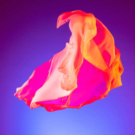 Flying piece of pink orange colored cloth texture. Transpparent piece of fabric flying isolated over purple studio backgroundの写真素材