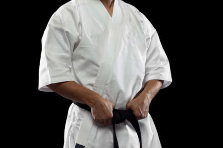 Cropped portrait of male sportsman in white kimono with black belt isolated over dark background