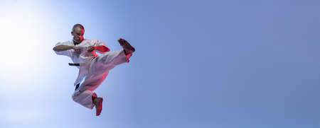 Young martial artist practicing flying kicks on gradient white blue background. Karate, judo, taekwondo sportの写真素材
