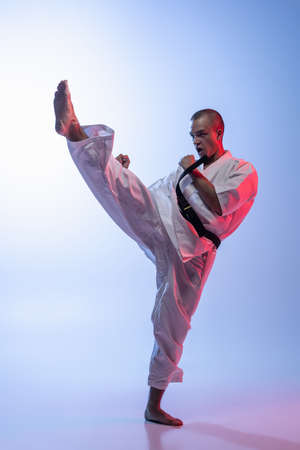 Portrait of caucasian man in kimono training martial art over gradient white blue background. Karate, judo, taekwondo sport.の写真素材