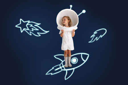 Creative artwork of little girl wearing astronaut helmet and standing on drawn rocket isolated over dark blue background with drawn asteroidsの写真素材