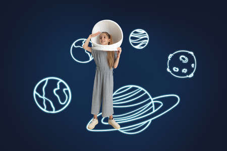 Creative artwork of little girl wearing astronaut helmet in space isolated over dark blue background with drawn planetsの写真素材
