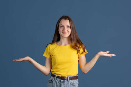 Close-up portrait of young beautiful girl wearing yellow shirt isolated over blue studio background