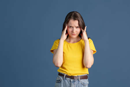 Cropped portrait of young beautiful girl wearing yellow shirt isolated over blue studio backgroundの写真素材
