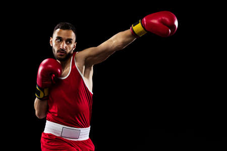 Cropped portrait of one professional boxer in red uniform training isolated over black background. Straight punchの写真素材