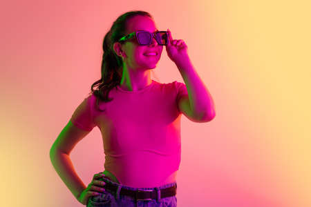 Cropped portrait of young caucasian girl in sunglases smiling isolated over gradient studio...