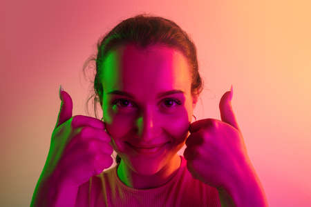 Close-up portrait of young girl with like gesture isolated over gradient studio background in neon lightsの写真素材
