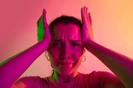Girl holding hands on her temples with isolated over gradient studio background in neon lights. Emotion of shockの写真素材