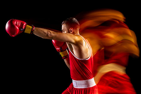 Cropped portrait of one professional boxer in red uniform training isolated over black background. Straight punch move. Mixed lightsの写真素材