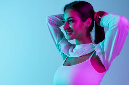 Side view cropped portrait of young beautiful girl isolated over blue background in neon light....