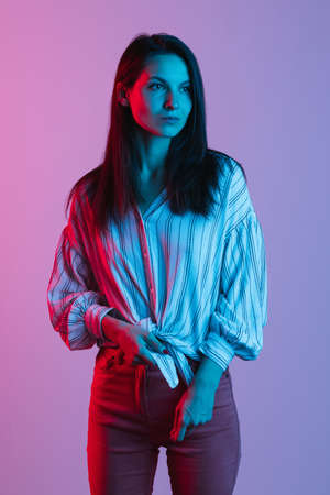 Cropped portrait of beautiful caucasian woman in casual clothes posing isolated over gradient pink purple background in neon lightsの写真素材
