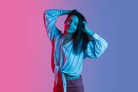 Portrait of young beautiful girl dancing isolated over gradient pink purple background in neon lightsの写真素材