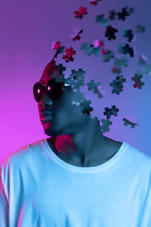 Creative collage of young african man in sunglasses looking away isolated over gradient purple background. Male head consist of puzzle piecesの写真素材