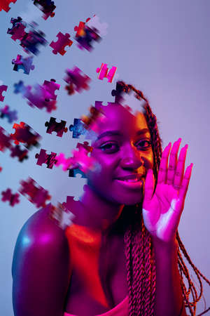 Creative collage of young african woman isolated over purple background in neon light. Female head consist of puzzle piecesの写真素材