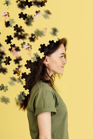 Modern collage of caucasian girl isolated over yellow background. Female head consist of puzzle pieces. Side viewの写真素材