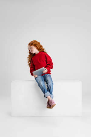 Portrait of little Caucasian girl, child with tablet posing isolated over gray studio background. Happy childhoodの写真素材