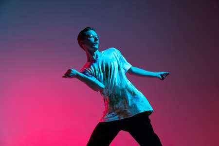 Cropped horizontal portrait of young male hip-hop dancer practising isolated over gradient pink purple background in neon lightの写真素材
