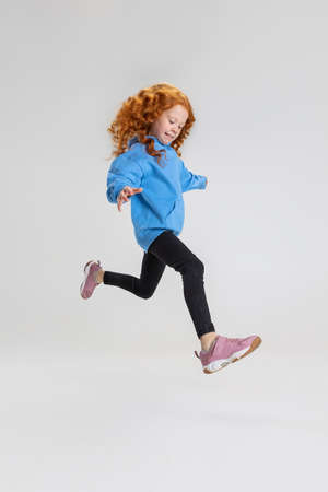 Portrait of little Caucasian girl, child jumping and posing isolated over gray studio background.