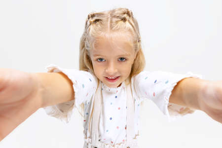 Portrait of little Caucasian girl, child posing, taking selfie isolated over white studio background.の写真素材