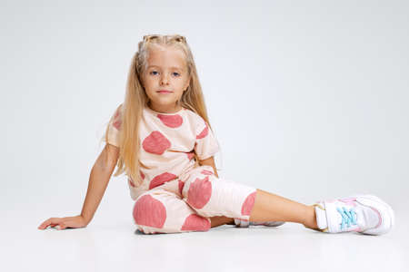 Full-length portrait of little Caucasian girl, child posing isolated over white studio background. Calmly sittingの写真素材