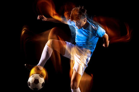 Full-length portrait of young sportsman, soccer football player training isolated over black background in mixed light. Attackerの写真素材